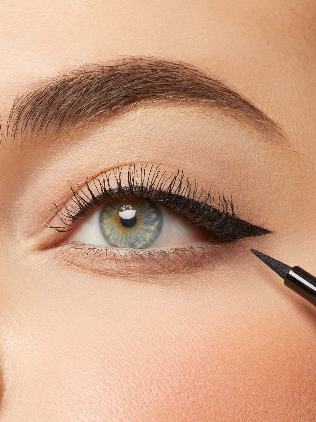 Close-up of an eye with eyeliner being applied, with a makeup pencil visible.