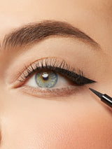 Close-up of an eye with eyeliner being applied, with a makeup pencil visible.