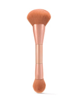 Dual-ended makeup brush with soft bristles; one end wide and fluffy, the other smaller and round. Held in a metallic handle, marked with Tarte, set against a white background.