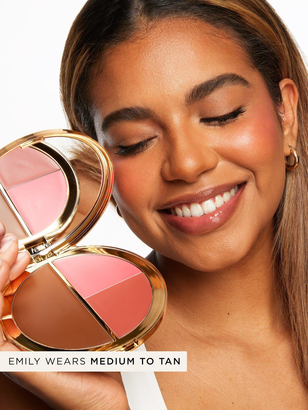 A smiling person holds a gold-cased Tarte Cosmetics palette with three shades against a white background. Text reads, Emily wears medium to tan.
