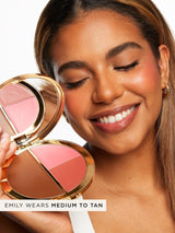 A smiling person holds a gold-cased Tarte Cosmetics palette with three shades against a white background. Text reads, Emily wears medium to tan.