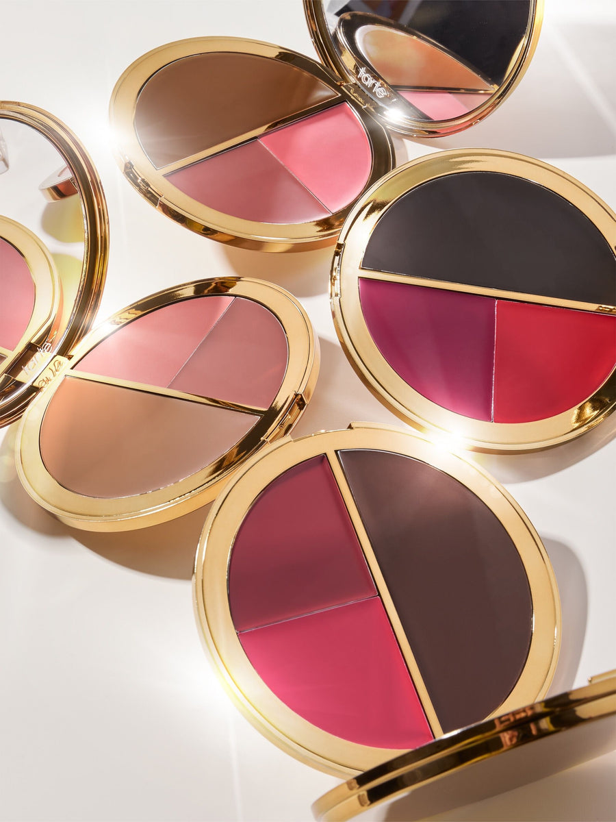 Compact makeup palettes with two sections of contrasting colors open to reveal shades of pink, brown, and red. Each palette features a reflective gold trim in a bright, well-lit setup. Text: tarte.