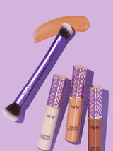 Makeup brush applying foundation swatch near three Tarte Cosmetics Shape Tape contour concealers on a light purple background. Tubes have patterned caps, displaying tarte and shape tape contour concealer correcteur contours.
