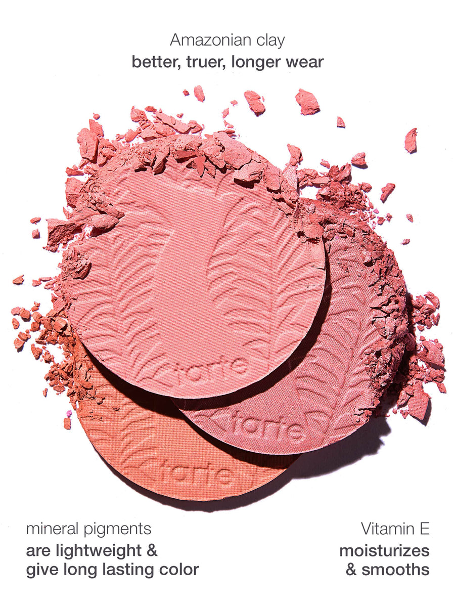 Three Tarte Cosmetics blush pans, embossed with leaf patterns, are scattered with pink powder on a white background. Text highlights Amazonian clay: better, truer, longer wear, mineral pigments: are lightweight & give long lasting color, and Vitamin E: moisturizes & smooths.