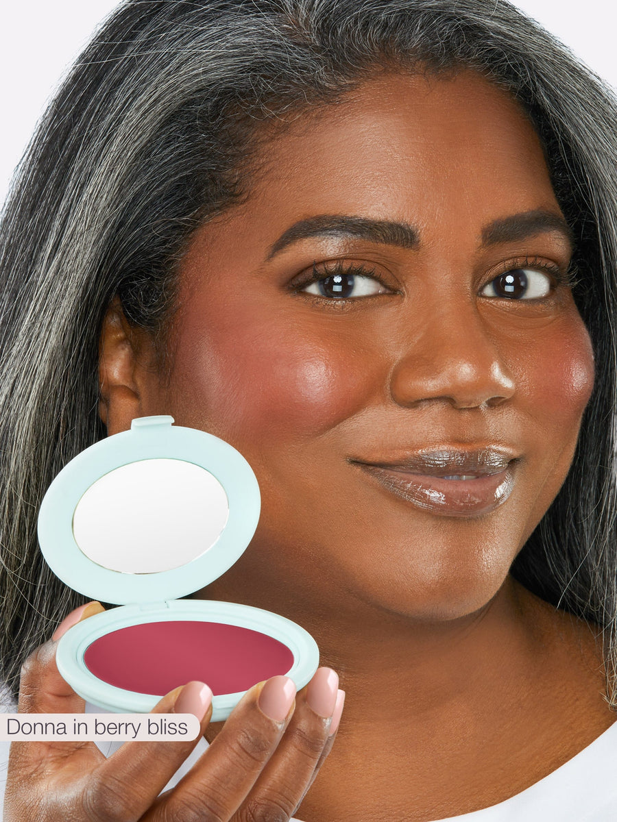 Woman holding a makeup compact with blush, showing the product on her face.