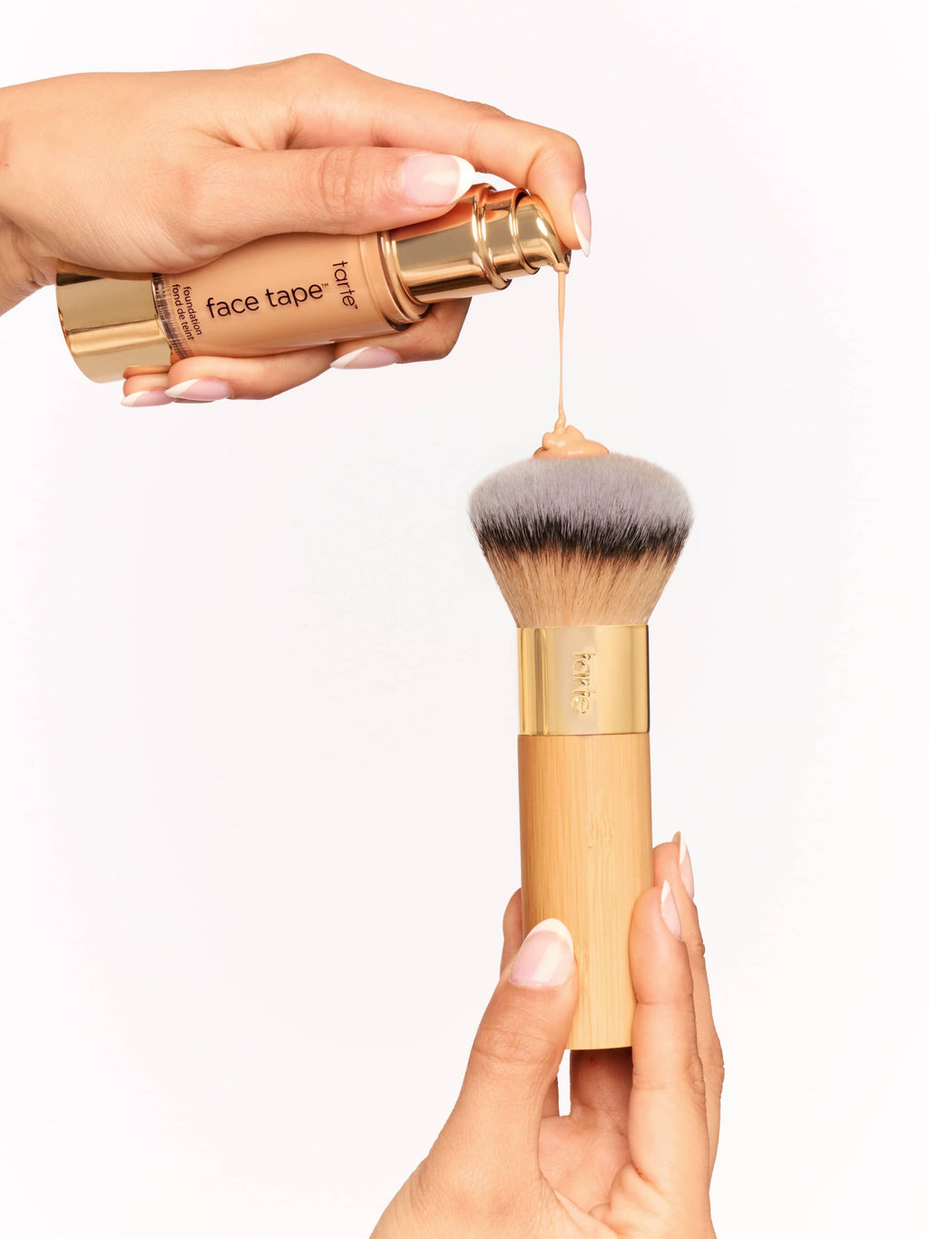 Makeup brush with a gold handle and gray bristle head, held by a hand against a white background.