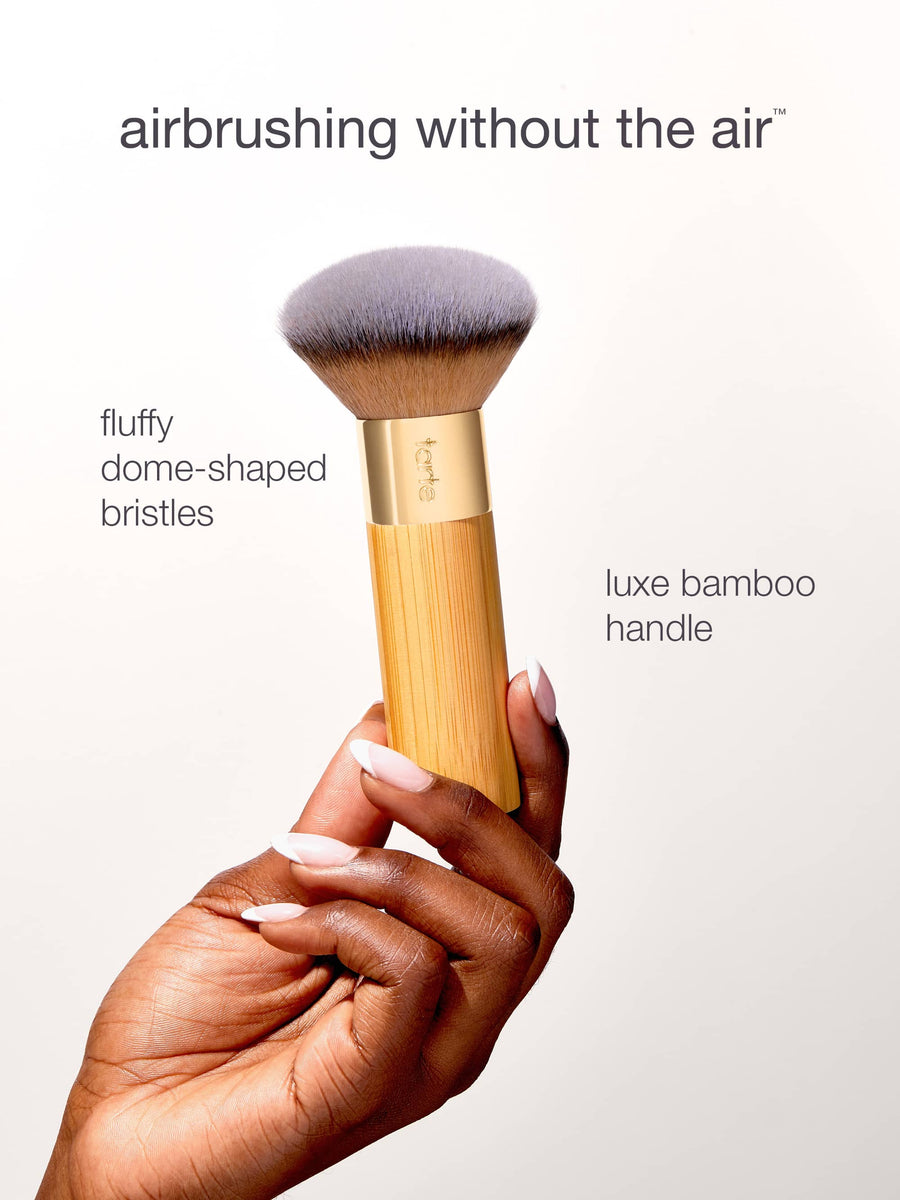 Makeup brush with fluffy dome-shaped bristles and luxe bamboo handle held by a hand.