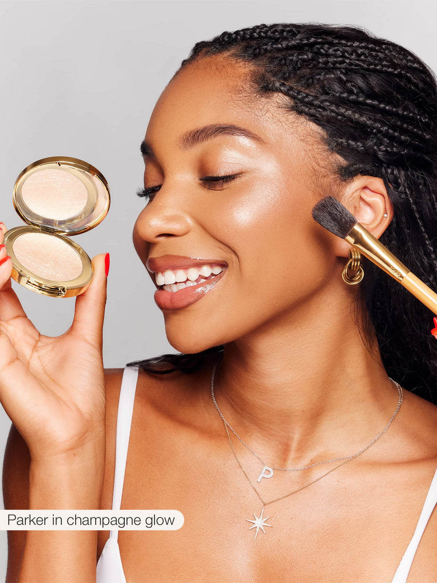 Woman applying makeup with a compact powder and brush, wearing a necklace.