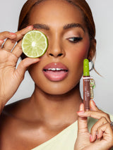 Woman holding a lime slice to her eye and a lip balm with a green cap.