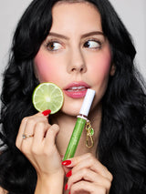 Woman holding a green lip balm and a lime wedge against a neutral background