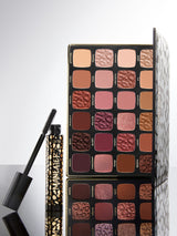 Makeup palette with various shades of eyeshadows and a mascara on a light gray background