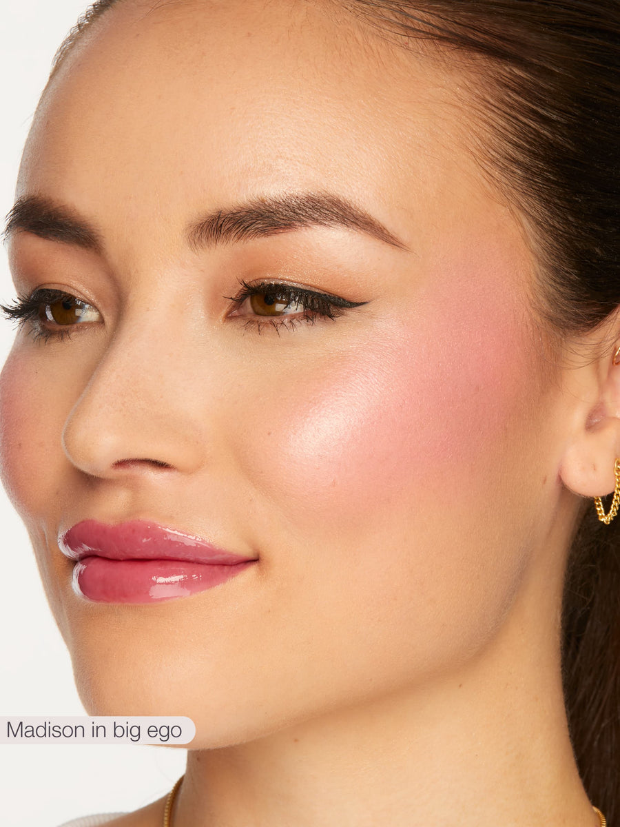 Close-up of a woman's face with pink blush on her cheeks, wearing pink lipstick and gold earrings.