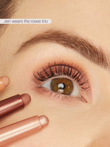 Close-up of a person's eye with makeup, holding two lipsticks, with text 'Jen wears the roses trio' above.