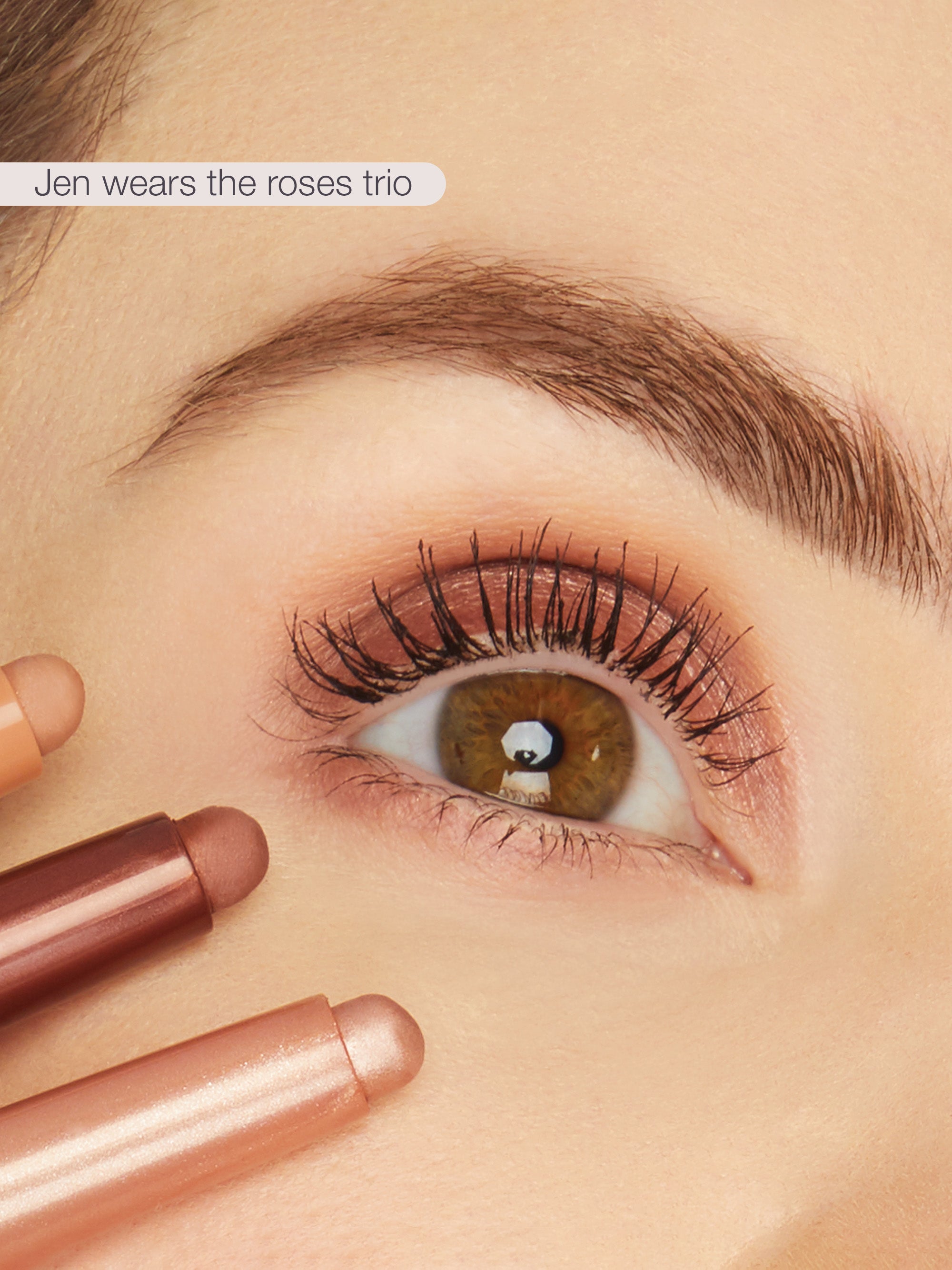 Close-up of a person's eye with makeup, holding two lipsticks, with text 'Jen wears the roses trio' above.