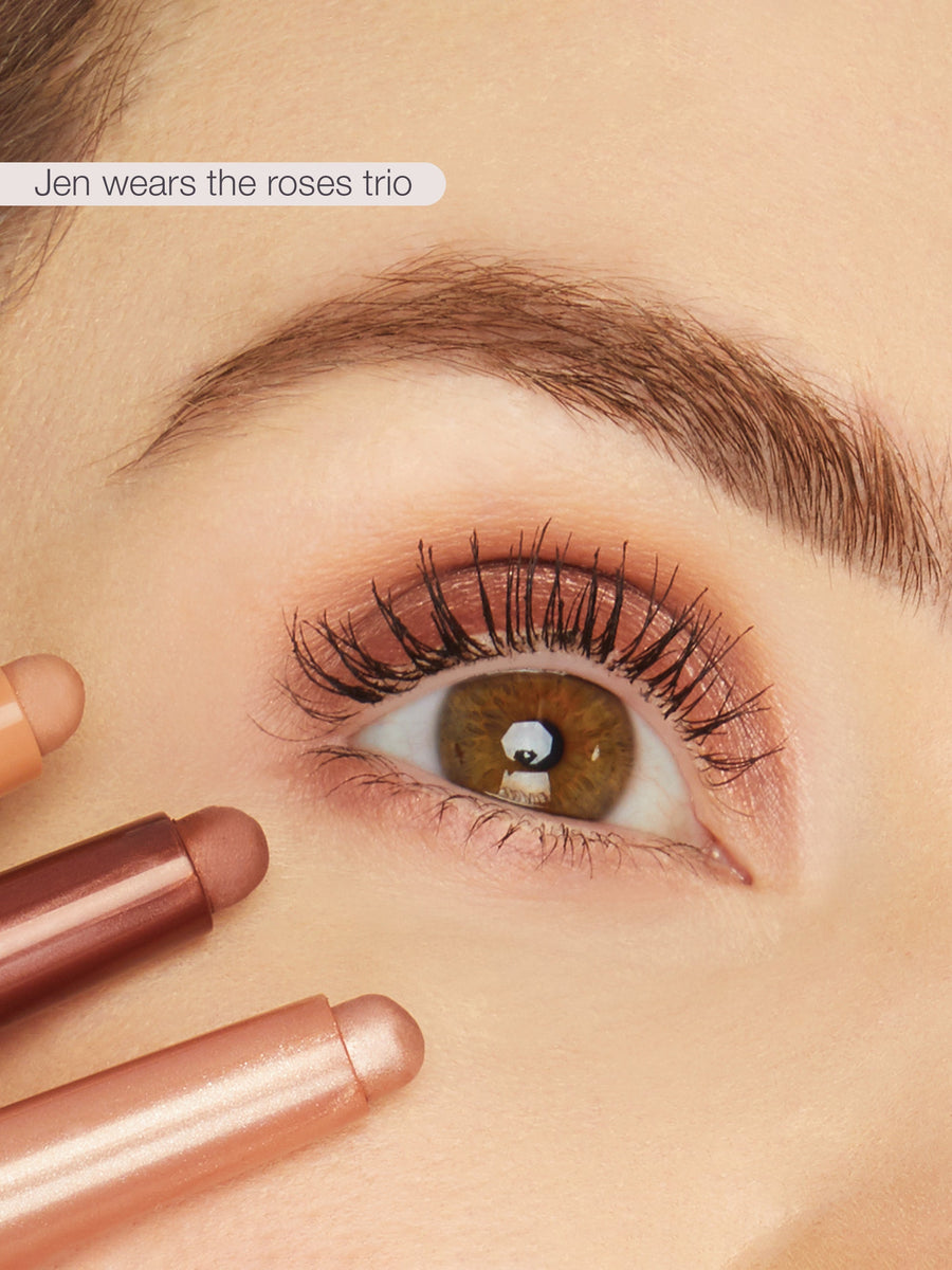 Close-up of a person's eye with makeup, holding two lipsticks, with text 'Jen wears the roses trio' above.