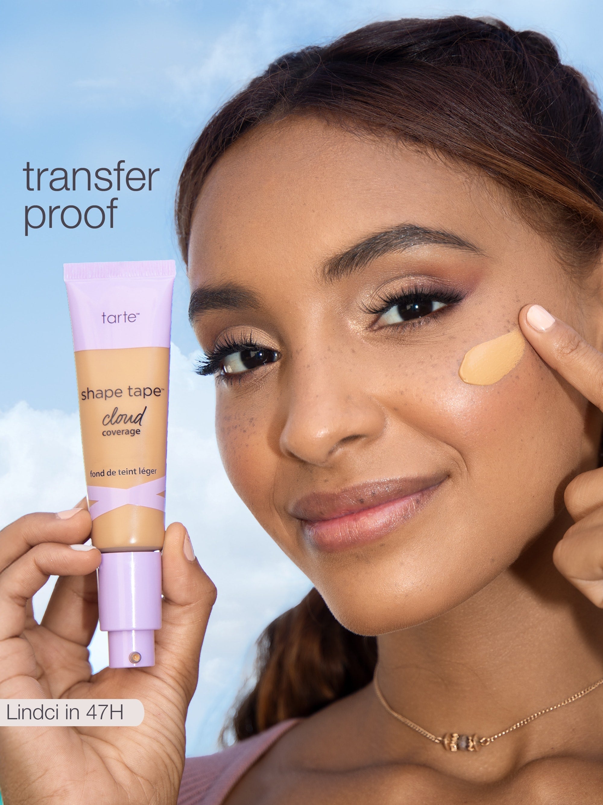 Woman applying tarte shape tape cloud cream to her face with a blue sky background