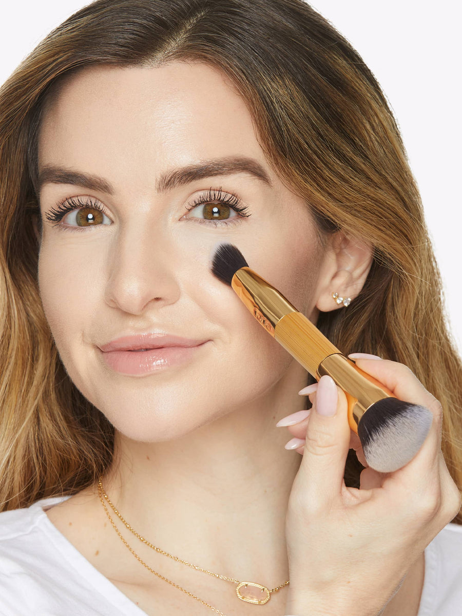 Woman applying makeup with a brush on a white background