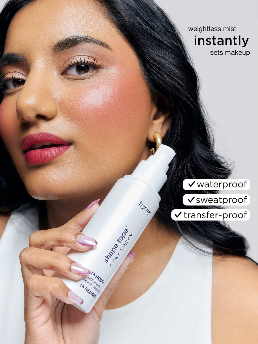 Woman holding a Tarte makeup spray with product features listed.