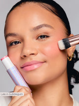 Woman applying makeup with a brush and stick, wearing gold earrings.