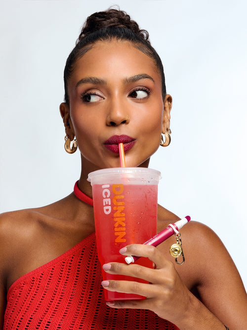 Woman holding a Dunkin' iced coffee cup with a straw against a plain background