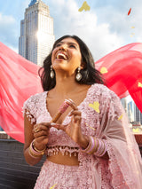 A woman joyfully holds a Tarte Cosmetics product while standing on a rooftop wearing a pink embellished outfit. Skyscrapers and vibrant red fabric create a dynamic city backdrop with fluttering petals.