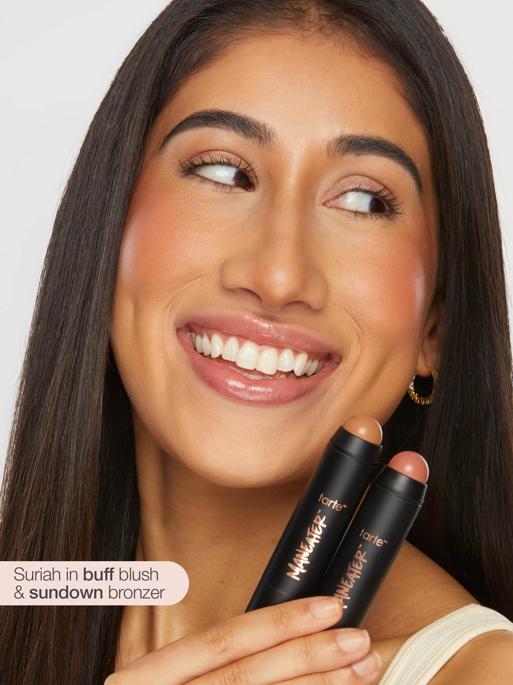 Woman holding tarte maneater cream bronze & blush stick duo with a plain background