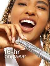 A person holds Tarte Cosmetics lights, camera, LASHES platinum mascara, smiling and winking. Text reads 16-hr longwear. The person has braided hair and wears a white top.