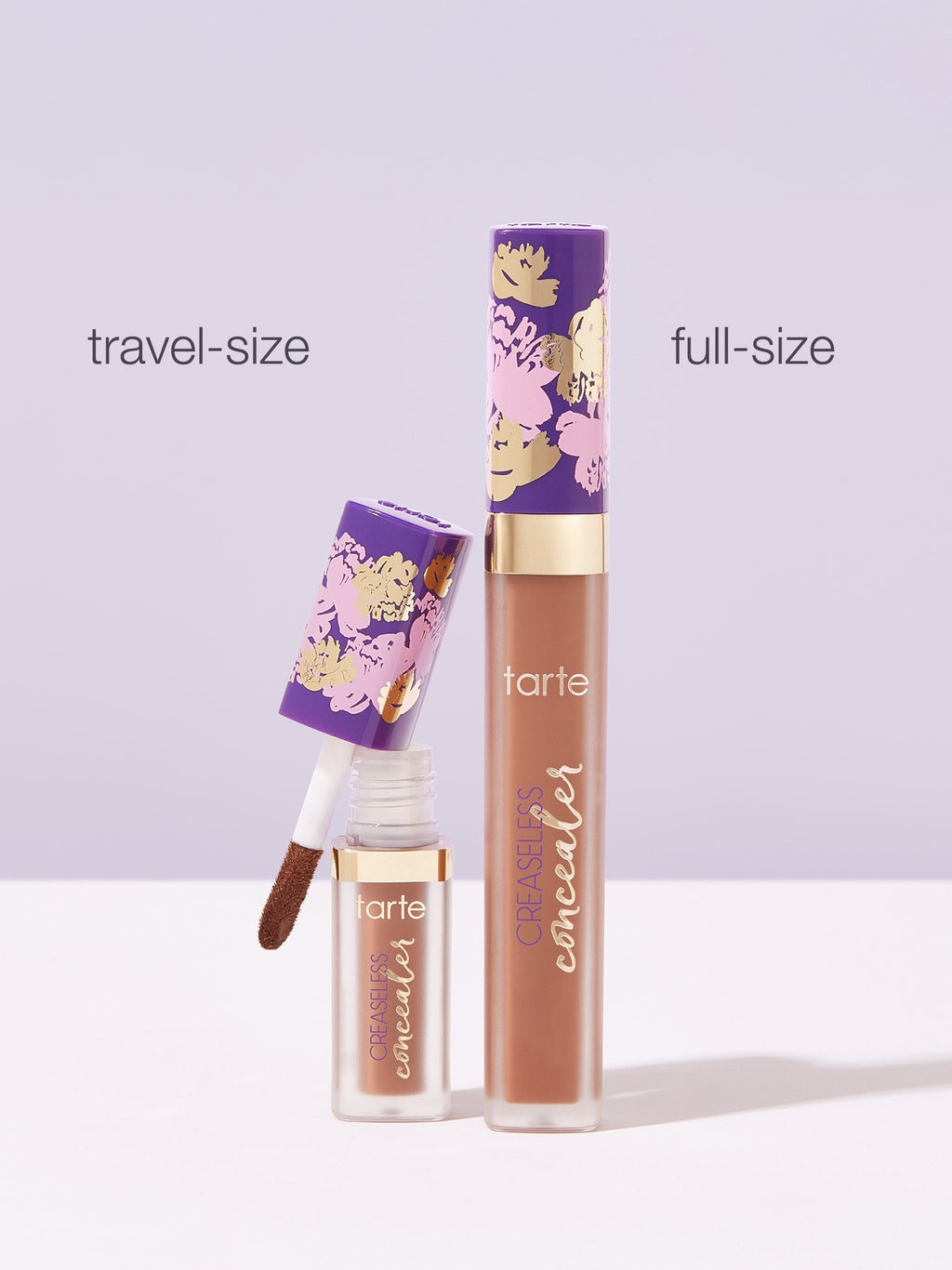 Two Tarte Cosmetics concealers, labeled travel-size and full-size, stand on a light surface. The travel-size concealer's applicator is visible. Both containers feature a purple floral design.