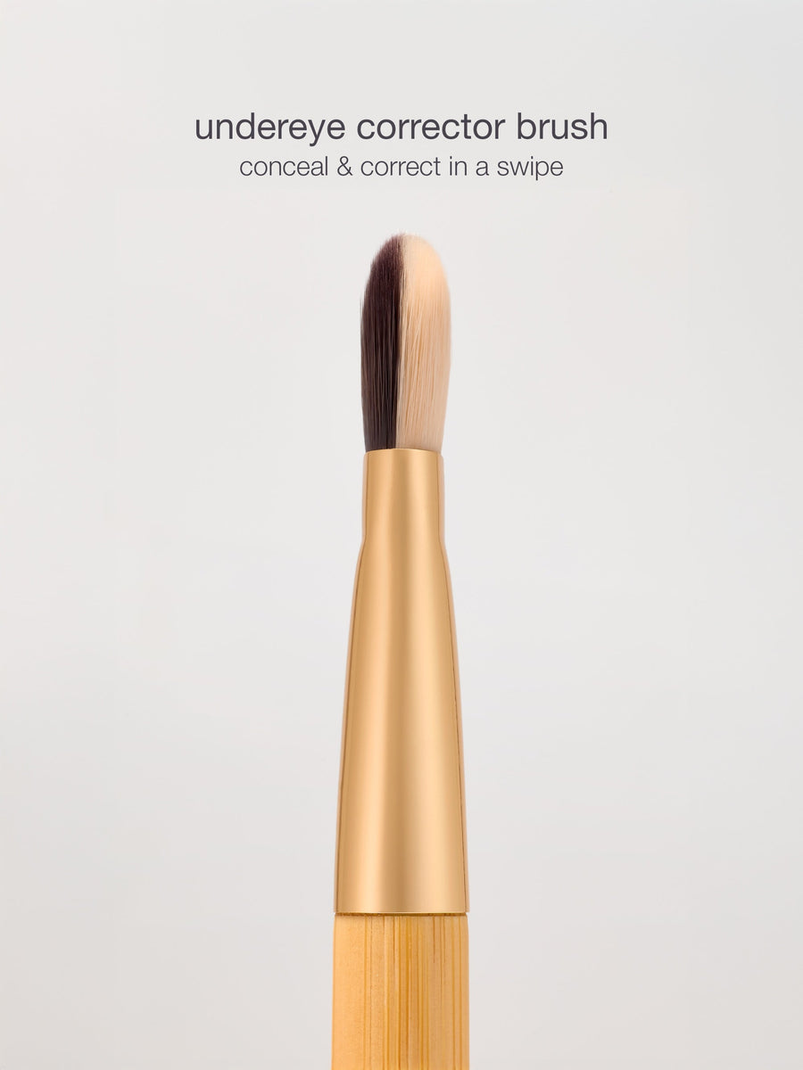 Undereye corrector brush with gold ferrule on a light gray background