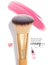Tarte makeup brush sits beneath a broad pink cream-blush stroke; two small stickers (heart, pink bottle) on a white background. Text: effortlessly hugs cheeks & melts cream blush tarte