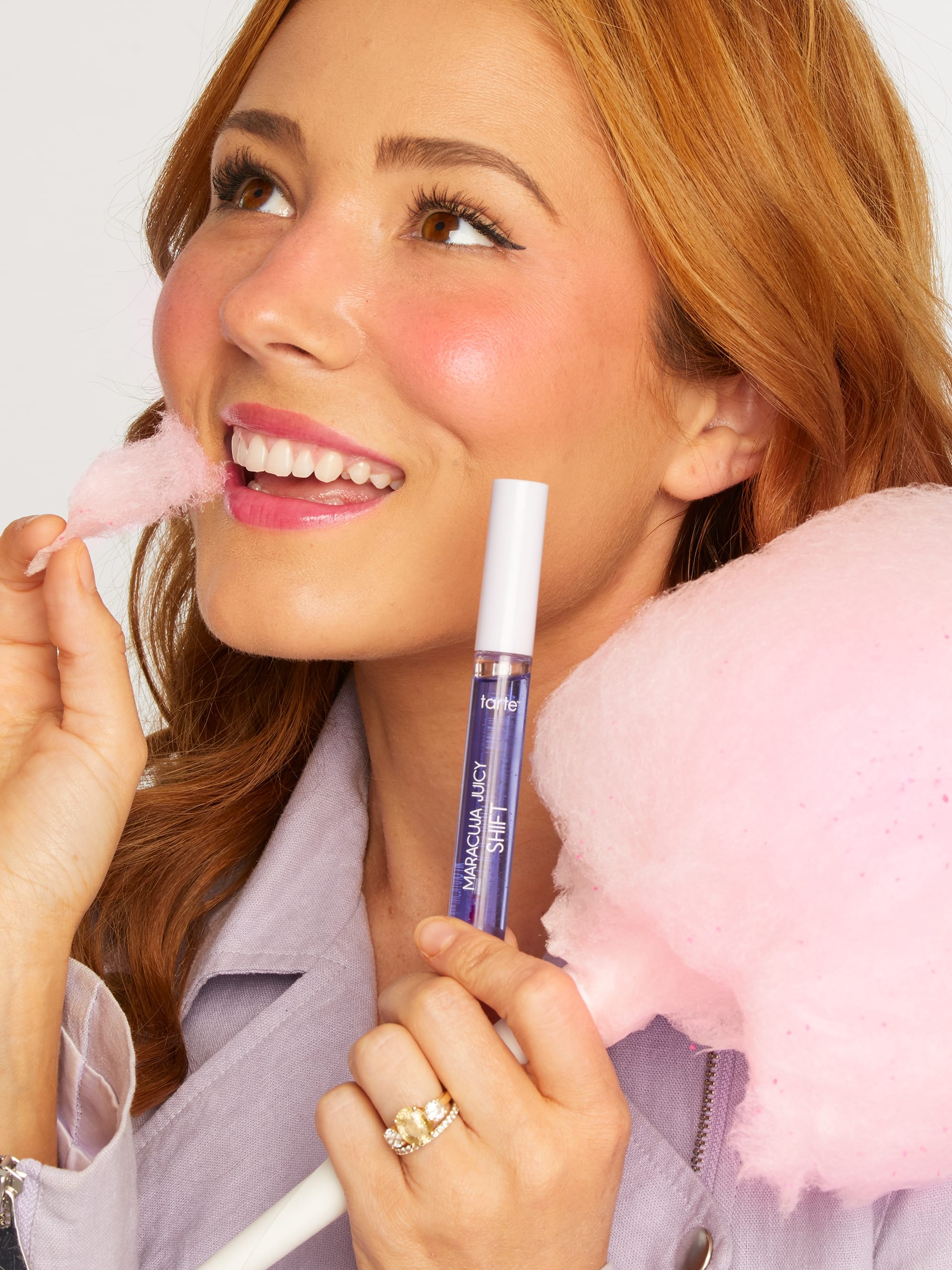 Woman holding pink cotton candy and a lip gloss with a white background