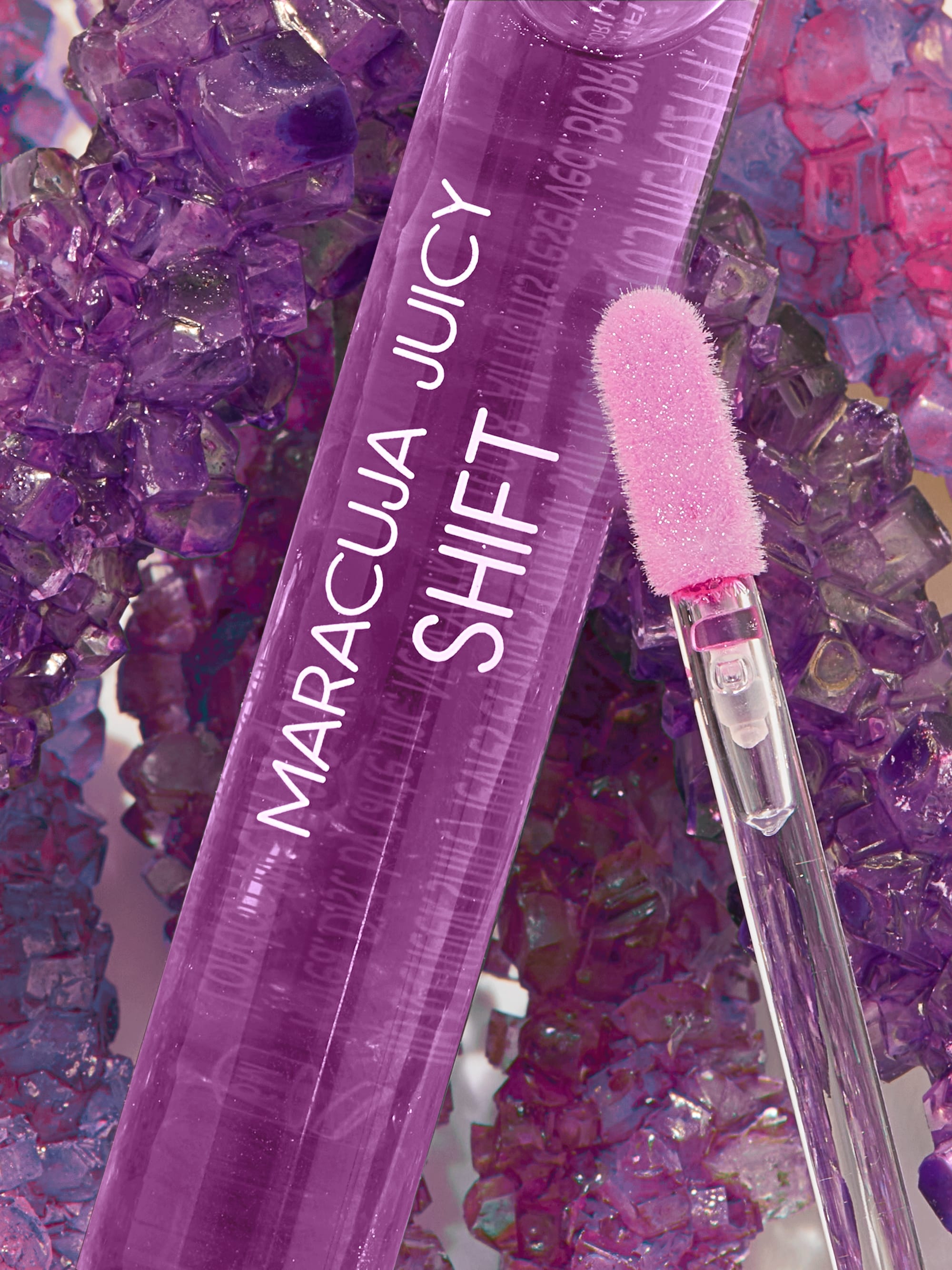 Purple lip gloss with a brush on a colorful gemstone background