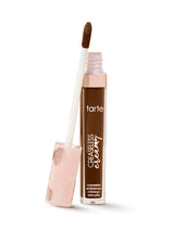 A tube of Tarte Cosmetics concealer with an applicator wand rests on a white surface. The tube is upright, and the wand, showing a brown concealer tip, leans against it.