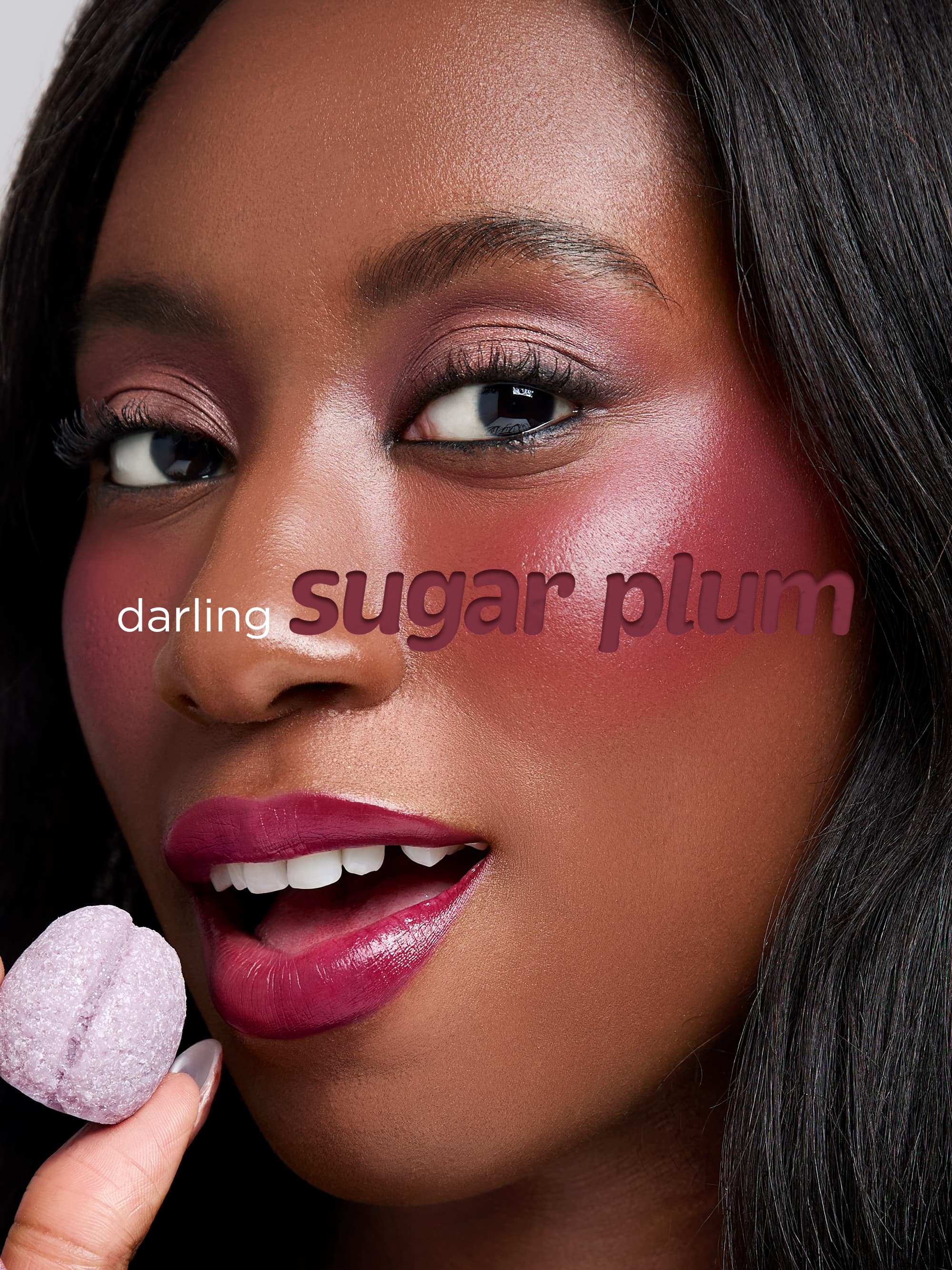 Close-up of a woman's face with 'sugar plum' makeup and a pink bath bomb.