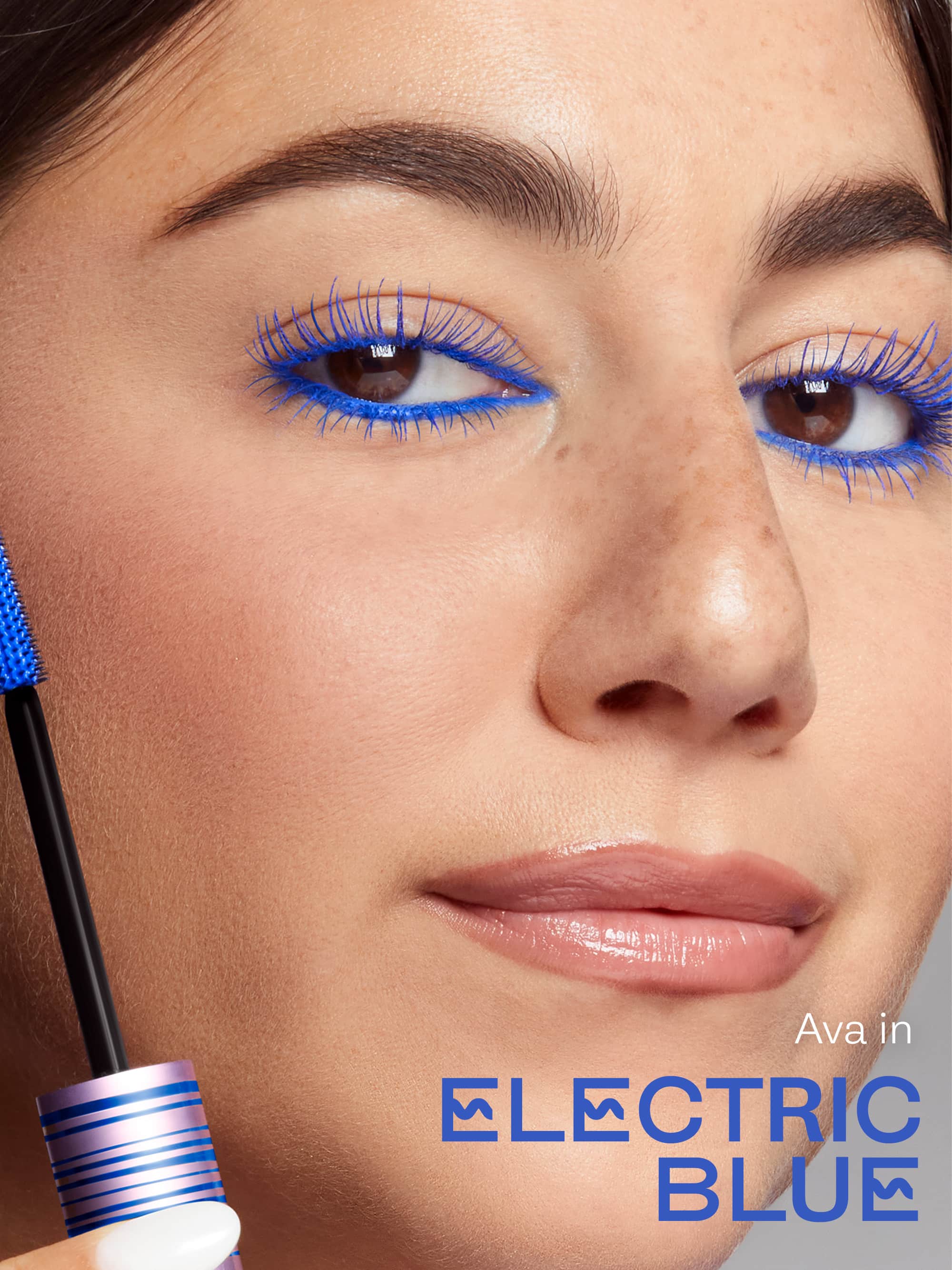 Close-up of a woman's face with blue eyeliner and mascara, with a blue mascara wand in the foreground.