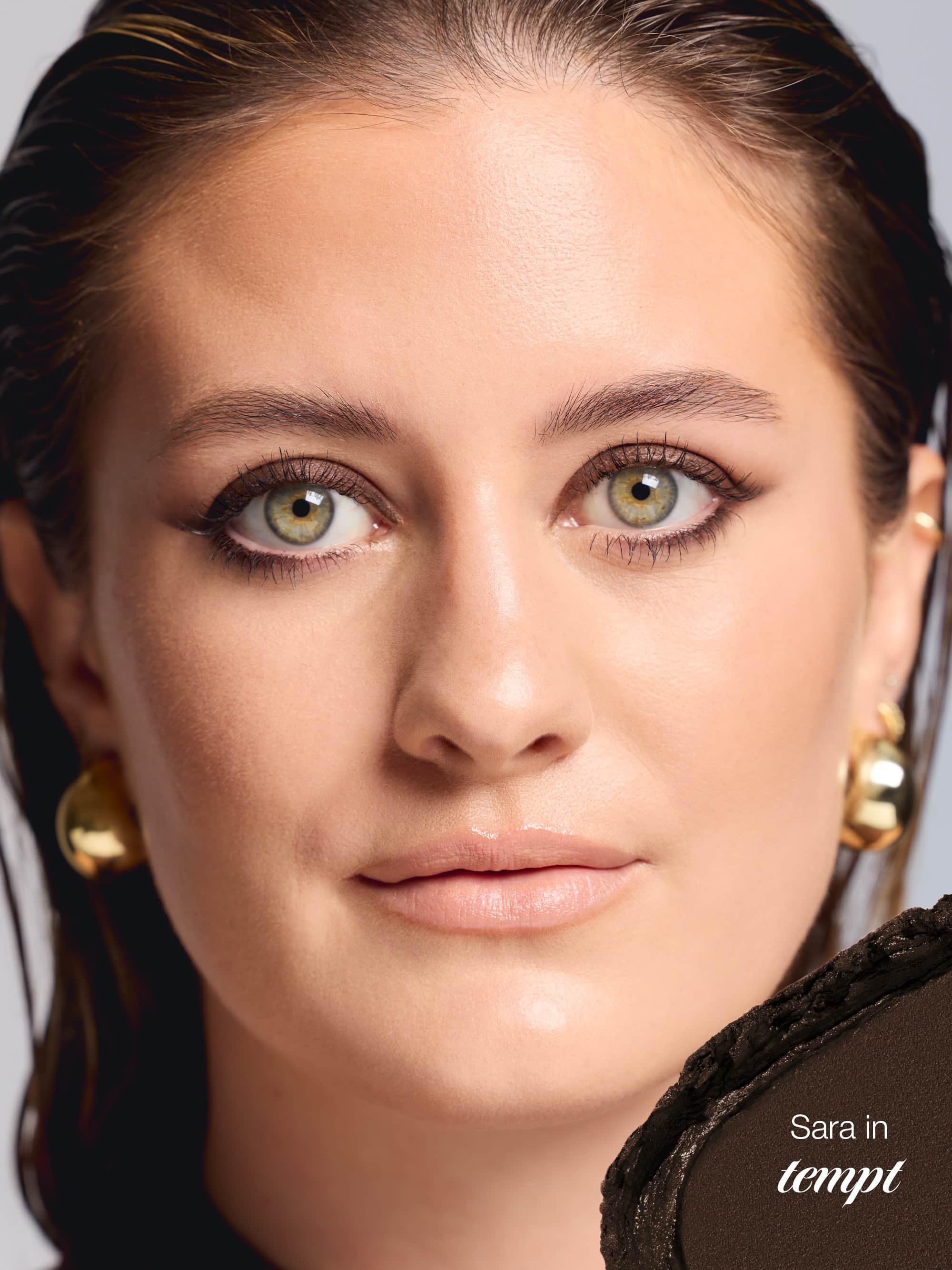 Close-up of a woman's face with gold earrings on a neutral background