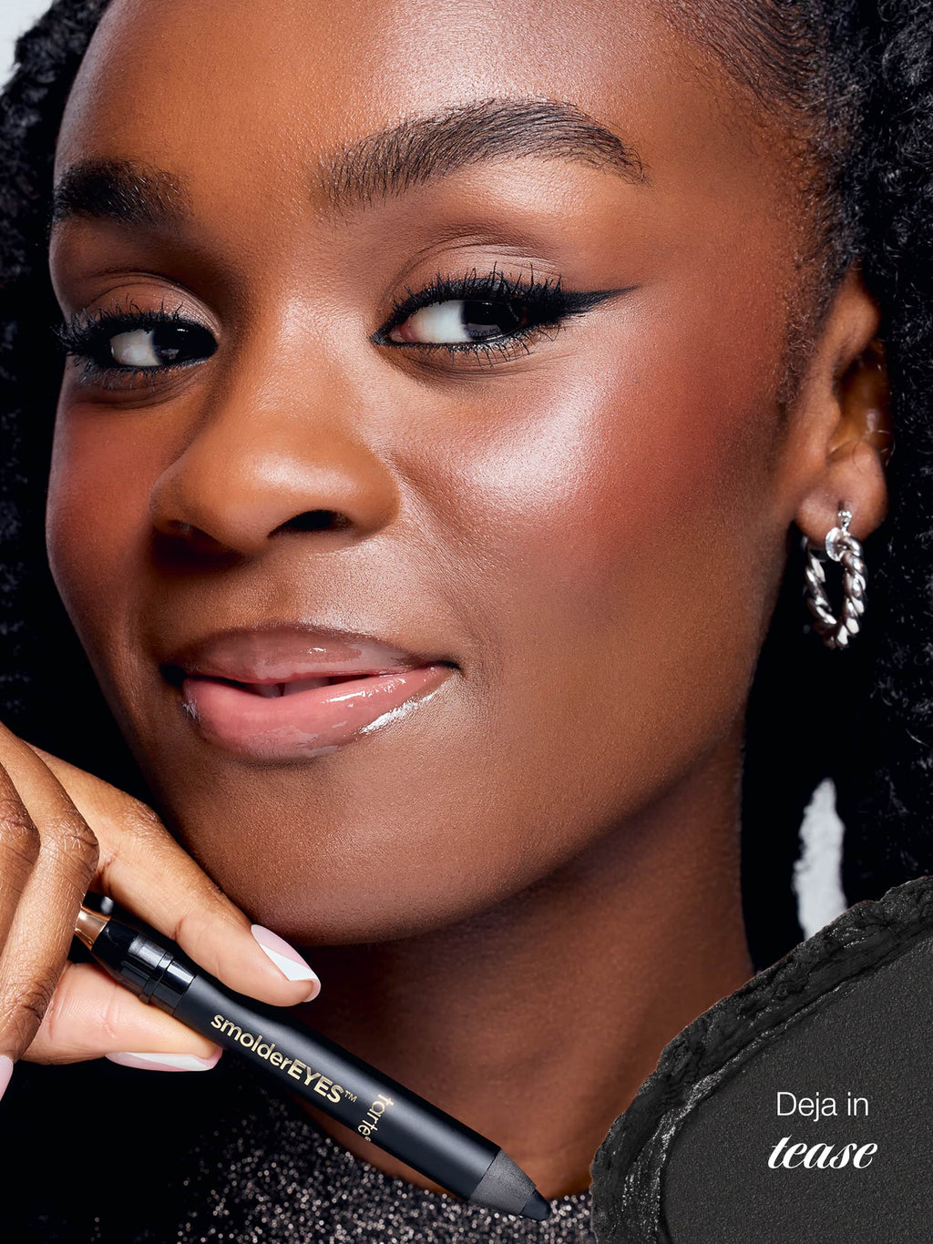Woman holding a makeup product with 'smolderEYES' branding, wearing earrings.