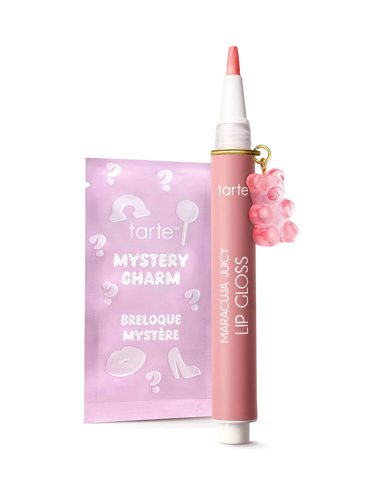 Tarte coral lip crayon with floral cap detail, uncapped to show the tip, resting beside a pink heart-patterned sachet on a white studio background.