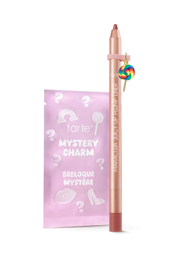 A rose-gold Tarte lip-liner pencil stands upright beside a pink sachet on a white background, a rainbow lollipop charm hanging from the pencil. Text: tarte; MYSTERY CHARM; BRELOQUE MYSTÈRE; MARACUJA JUICY LIP PUMP LINER
