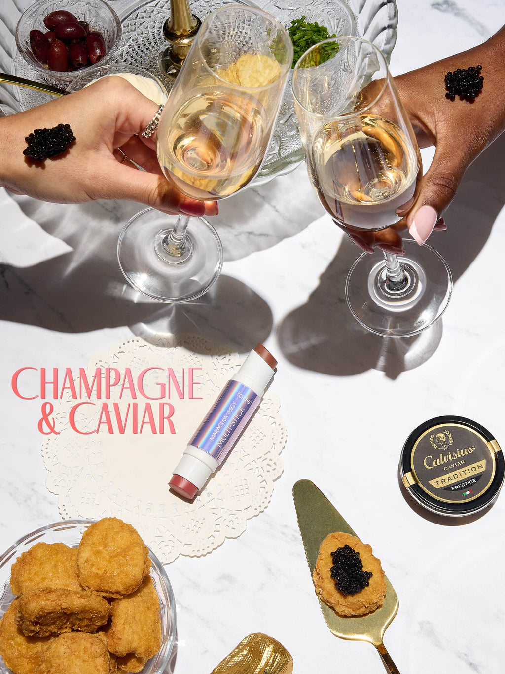 Two hands holding champagne glasses with caviar on a table setting, featuring tarte maracuja juicy double ended multi stick 