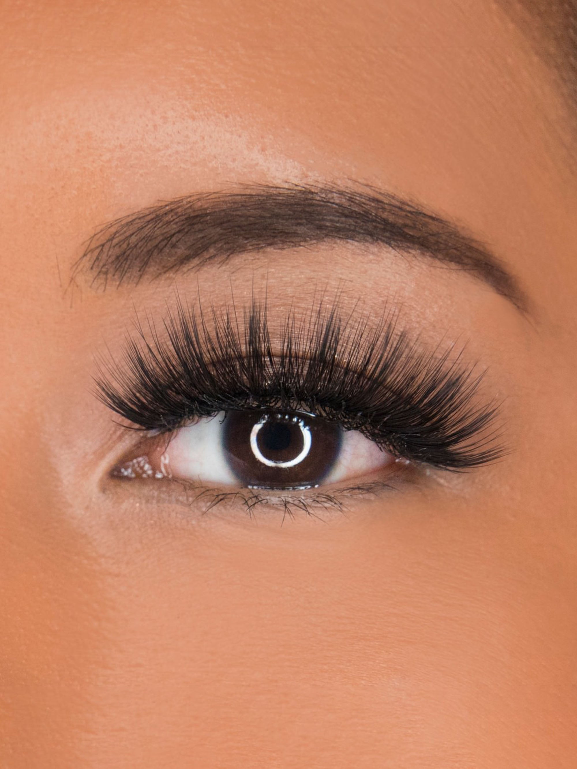 Close-up of an eye with long, dark eyelashes on a neutral background