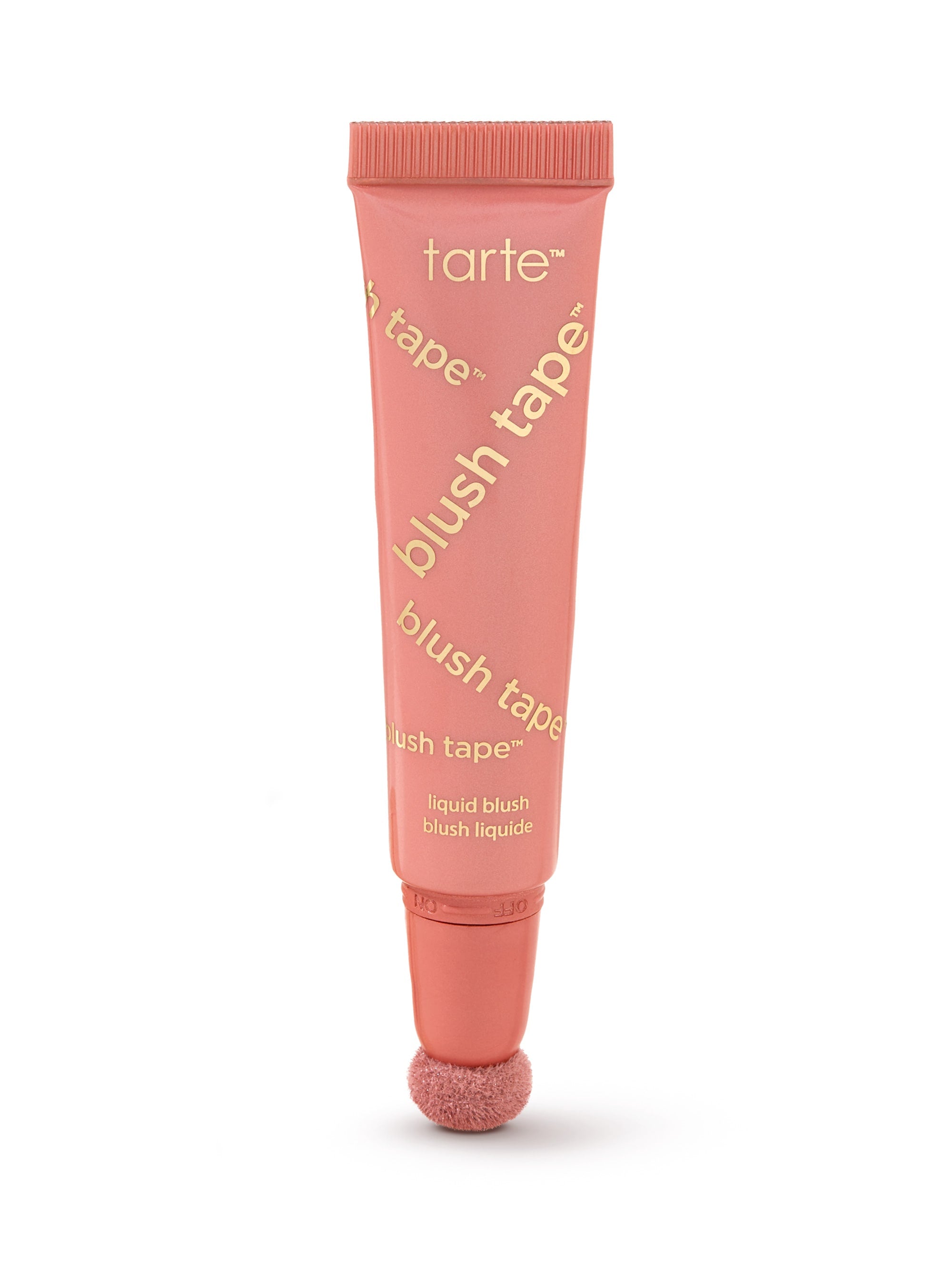 A coral-pink Tarte blush tube stands upright, applicator sponge at the base, on a white background. Text visible: tarte; blush tape™ (repeated diagonally); liquid blush; blush liquide.