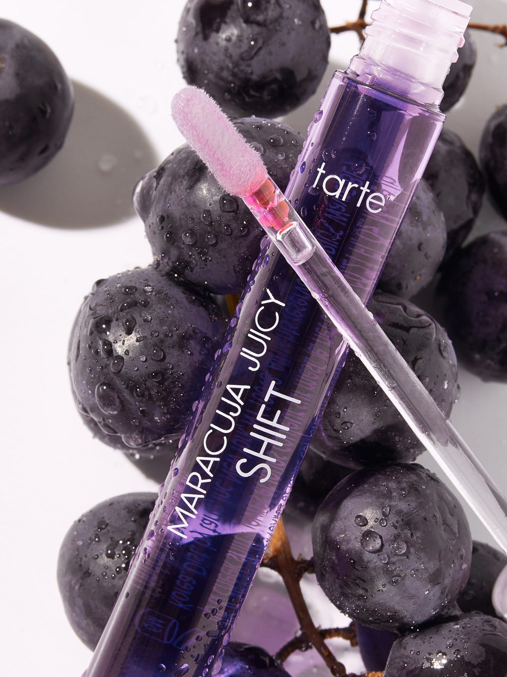 Tarte Maracuja Juicy Shift lip gloss with grapes on a white background