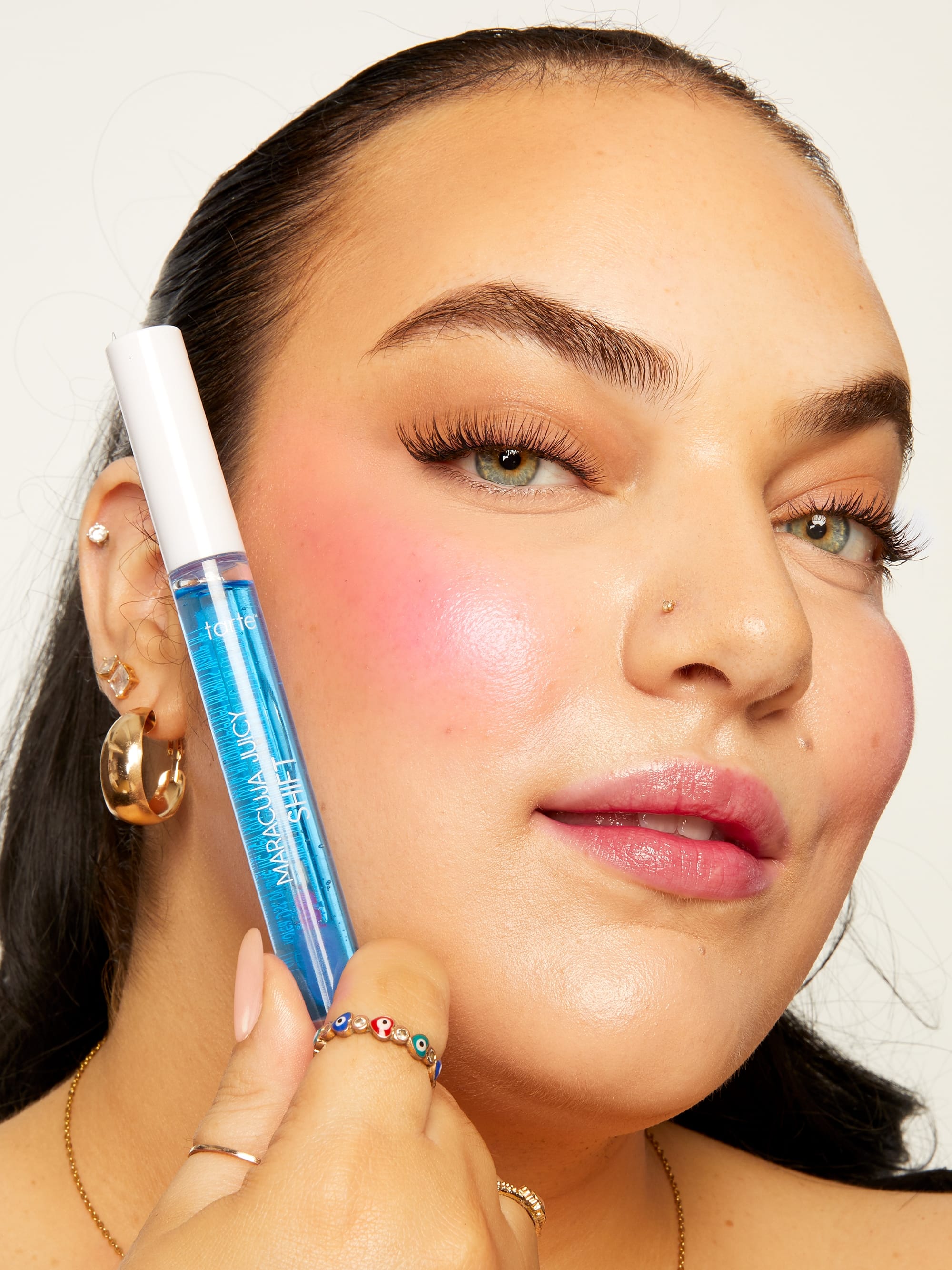 Woman holding a makeup product close to her face against a neutral background